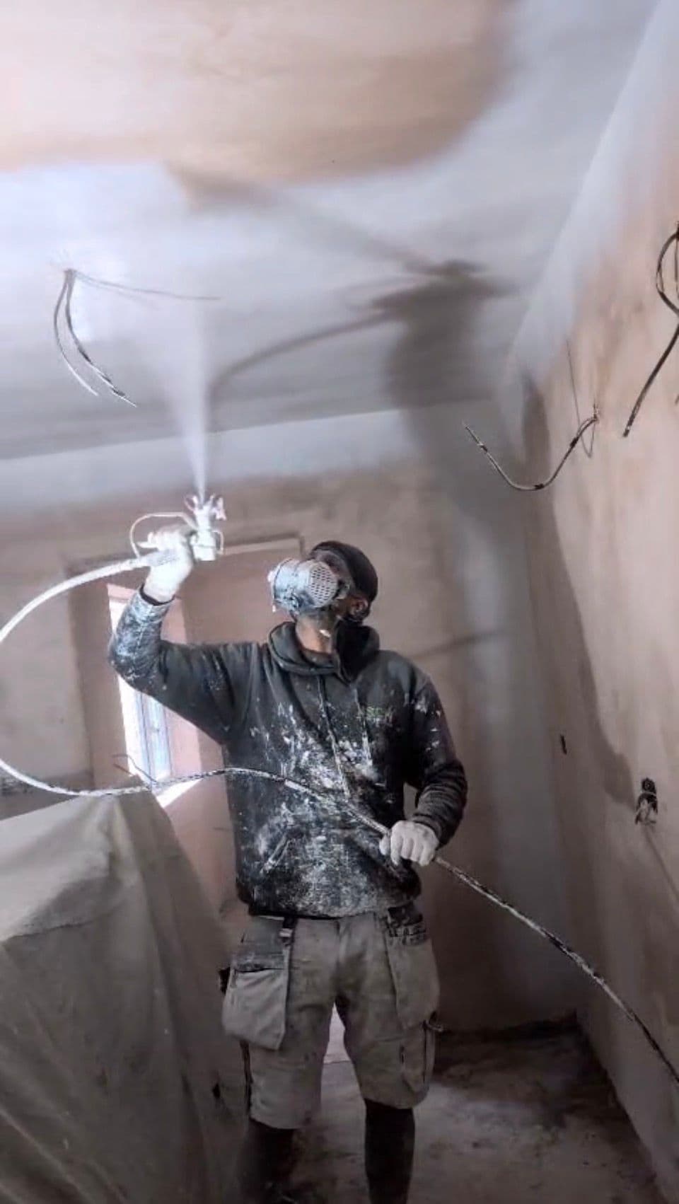 Worker spray painting ceiling with airless sprayer and respirator mask