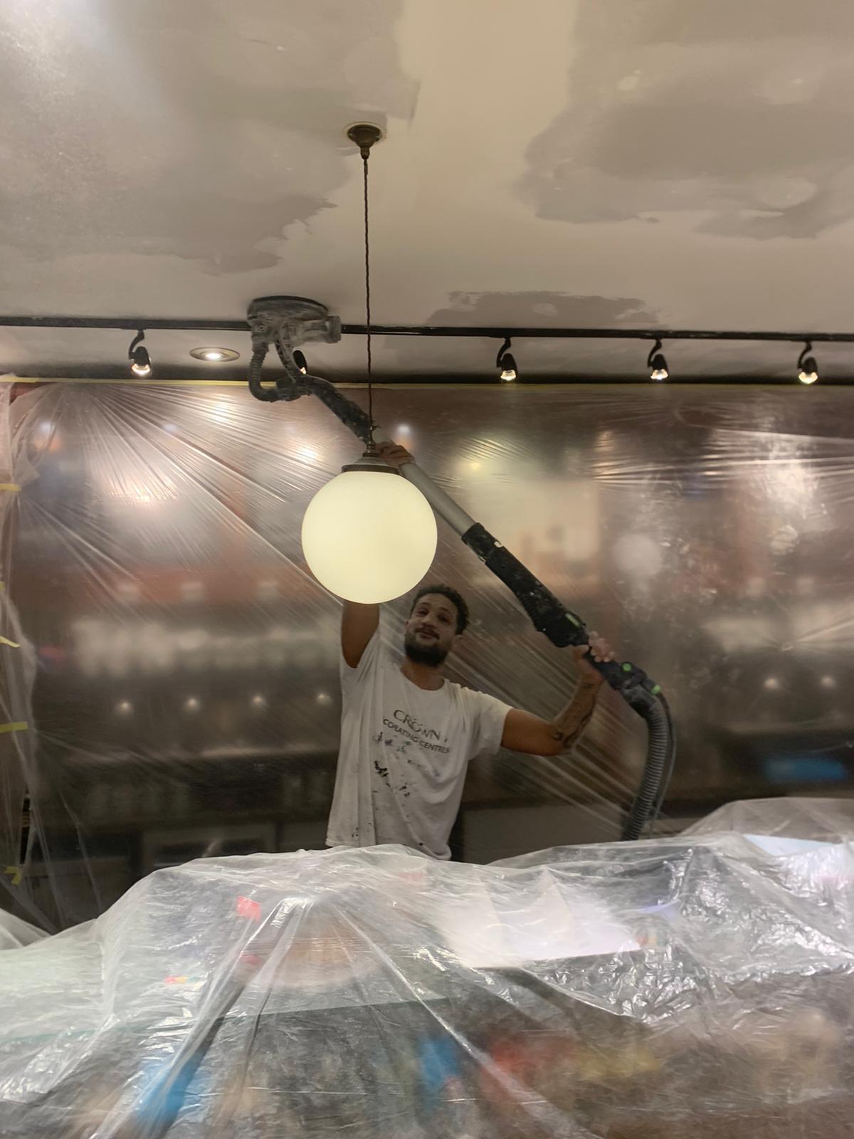 Worker using drywall sander with dust extraction during ceiling prep