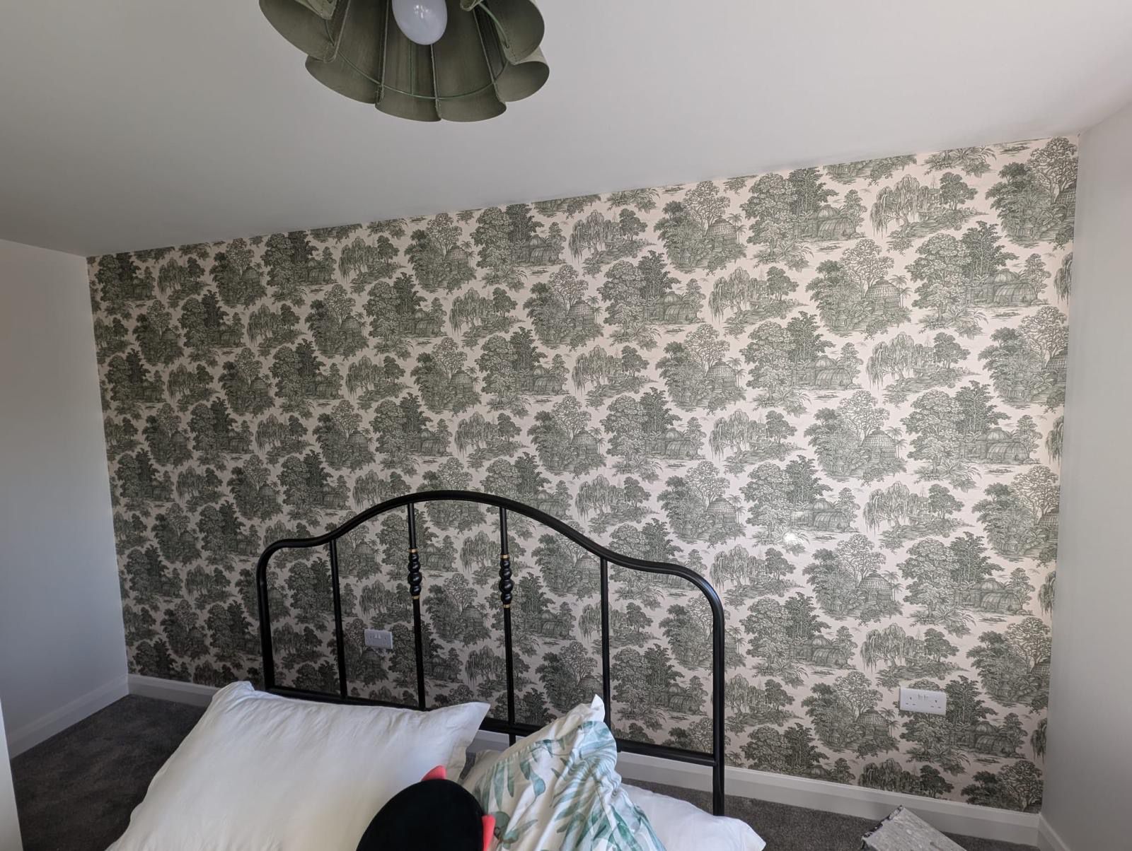 Bedroom with green toile wallpaper behind iron bed frame