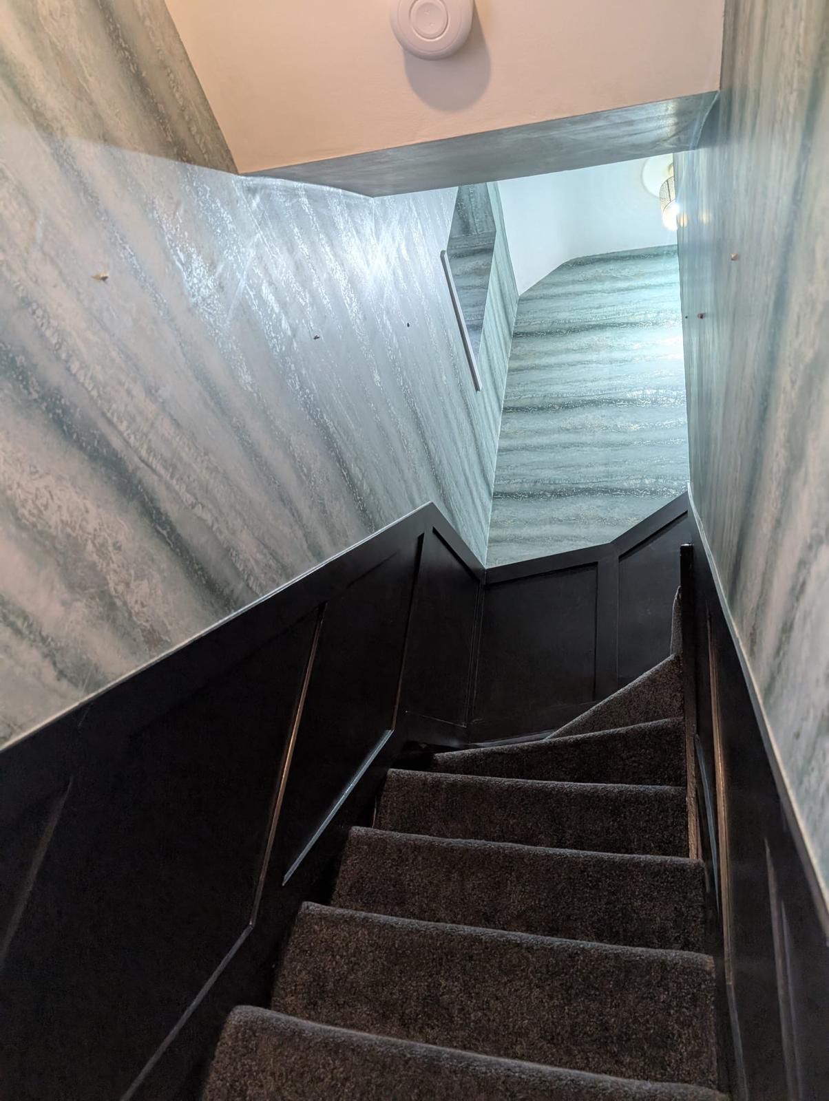 Staircase with marble effect wallpaper and dark painted panelling
